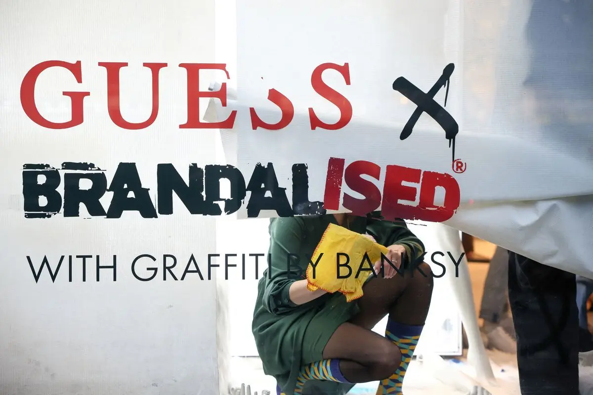 Employees remove lettering from a window display inside the flagship Guess store